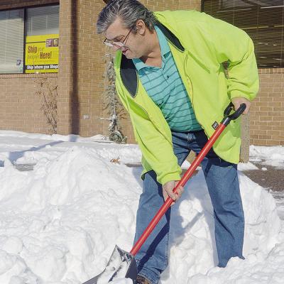 Chan Martin goes in and out of S&amp;D Drug, while using a shovel to clear the sidewalk of snow, in hopes of fighting the cold temperatures Monday morning. CDN | Micah Ashcraft