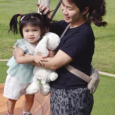 Audrey Nguyen, left, balances on the swing as Anh Dao helps her stand up Wednesday at the McLain Rogers Park Playground. CDN | Christian Jacobsen