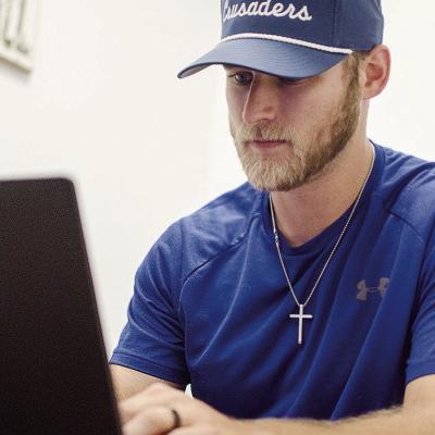 CDN | Sam Goodwyn New Corn Bible Academy football coach Peyton McNutt gets some work done Monday in his office.