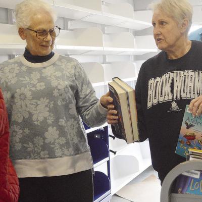 Western Plains Library System Board Members Carlotta England, left, and Kay Hagerman pass each other stacks of books while stocking the shelves of the new WPLS bookmobile. CDN | Micah Ashcraft