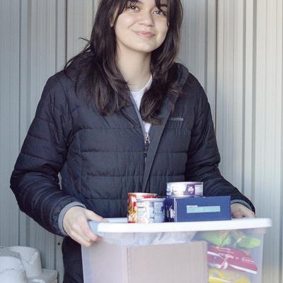 Carys Garcia carries a stack of donated food to the community food box she set up behind the Garcia Law offices Wednesday morning. CDN | Micah Ashcraft