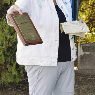 Linda Ford displays the awarded plaque of Mary Ford recognizing 50 years of service to the Greyhound Bus line for the 2026 Spring Cemetery Walk at the Clinton Cemetery. CDN | Christian Jacobsen
