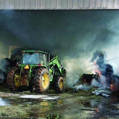 A tractor works to remove hay bale debris Tuesday morning at Tim Davis’ barn located on N. 28th Street The Clinton Fire Department responded to the hay bale barn fire and it is estimated more than 500 bales ignited in the blaze. CDN | Courtesy photo