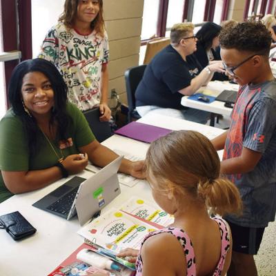 Kimberly Hurd, left, Dadrian Hester, Maylazia Hester and Tradarius Hester give out supplies at enrollment Tuesday at the Clinton Middle School Cafeteria. CDN | Caleb Blanchard School supplies listed for CPS