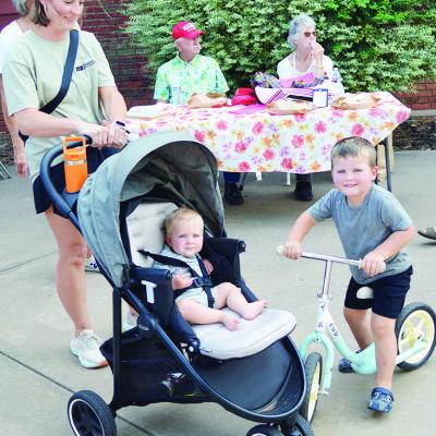 From left, front, Kassy, Bowen, and Barrett Bonham visit the Farmers Market and enjoy the sun Thursday at Engleman Park. In the back, Bill Hayes and Judy “The Pie Lady” Hayes sell their desserts. CDN | Christian Jacobsen