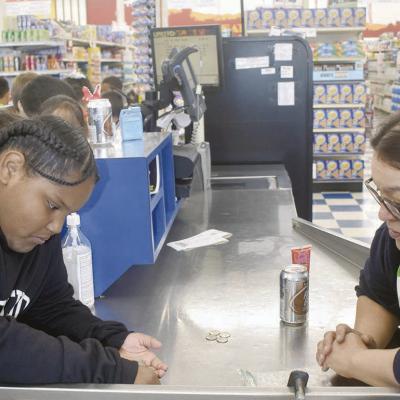 Jazzlyn Douglas, left, a student at Southwest Elementary, counts exact change to pay Leti Contreras, a United Store employee, for soda and candy during a walking field trip. The purchase, made with coins, is part of a lesson on counting change. CDN | Elis Change for soda