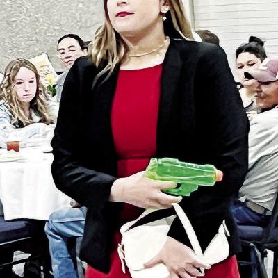 Mock trial member Kinsley Bridges, playing the role of Miss Scarlett in an adapted version of “Clue,” shows her “murder weapon” Monday night at the Frisco Center. CDN | Michael Maresh