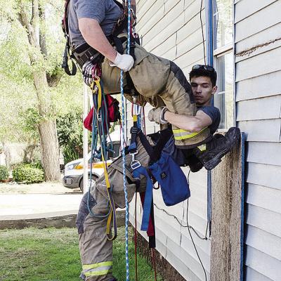 Clinton firefighter Austin Long, top, helps lower fellow firefighter Ben Switzer down during training at the Mission House.