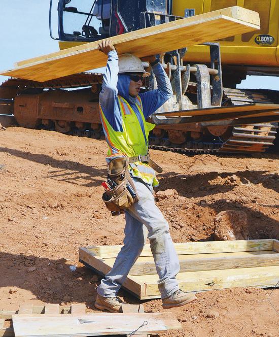 Antonio Garnica carries the next panel to create a box frame for a future concrete support beam Wednesday during construction on Red Wheat Drive. CDN | Christian Jacobsen
