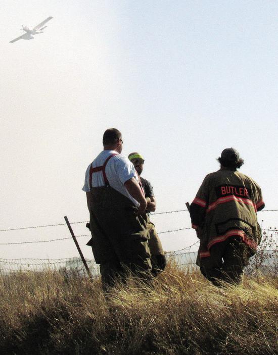 Area firefighters Isac Shephard, Cody Jeffrey, and Joel Barnett stand at the ready, as a “super scooper” plane flies to Foss Lake to refill Wednesday afternoon near Butler. CDN | Christian Jacobsen