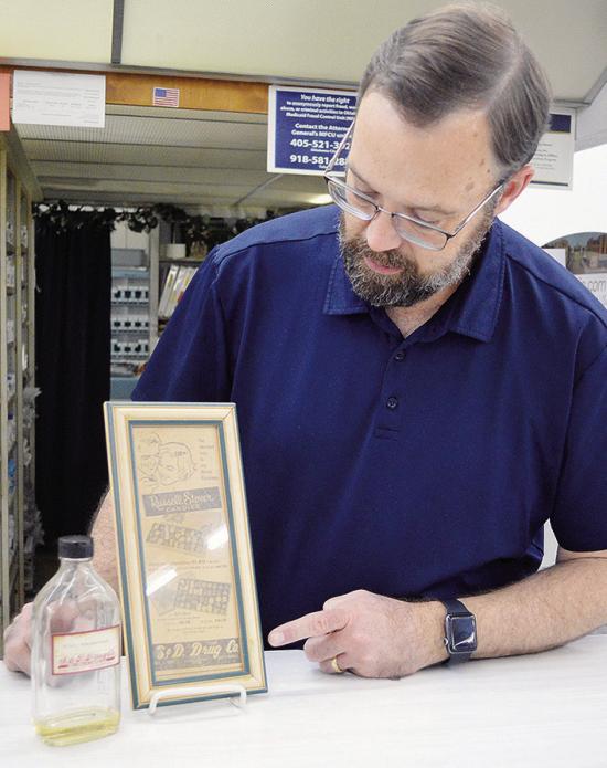Scott Campbell points out the S&amp;D Drug logo on a vintage advertisement and bottle while discussing the 133-year history of the business in Clinton. CDN | Micah Ashcraft