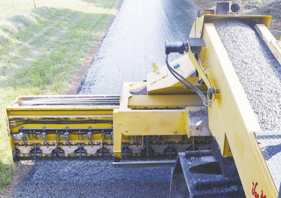 A Rock chipper spreads gravel on a layer of oil to become the first layer of a paved street at N. 2260 Road. CDN | Christian Jacobsen A Rock chipper spreads gravel on a layer of oil to become the first layer of a paved street at N. 2260 Road. CDN | Christian Jacobsen